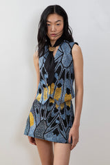 A model wearing a fitted hand-embroidered blue and black vest with hip-length design, made from smocking cotton.