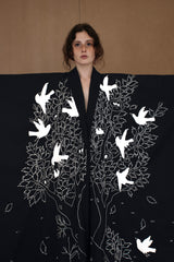 A person wearing a reversible hand-embroidered double face coat with white embroidery depicting birds and leaves on a dark background.